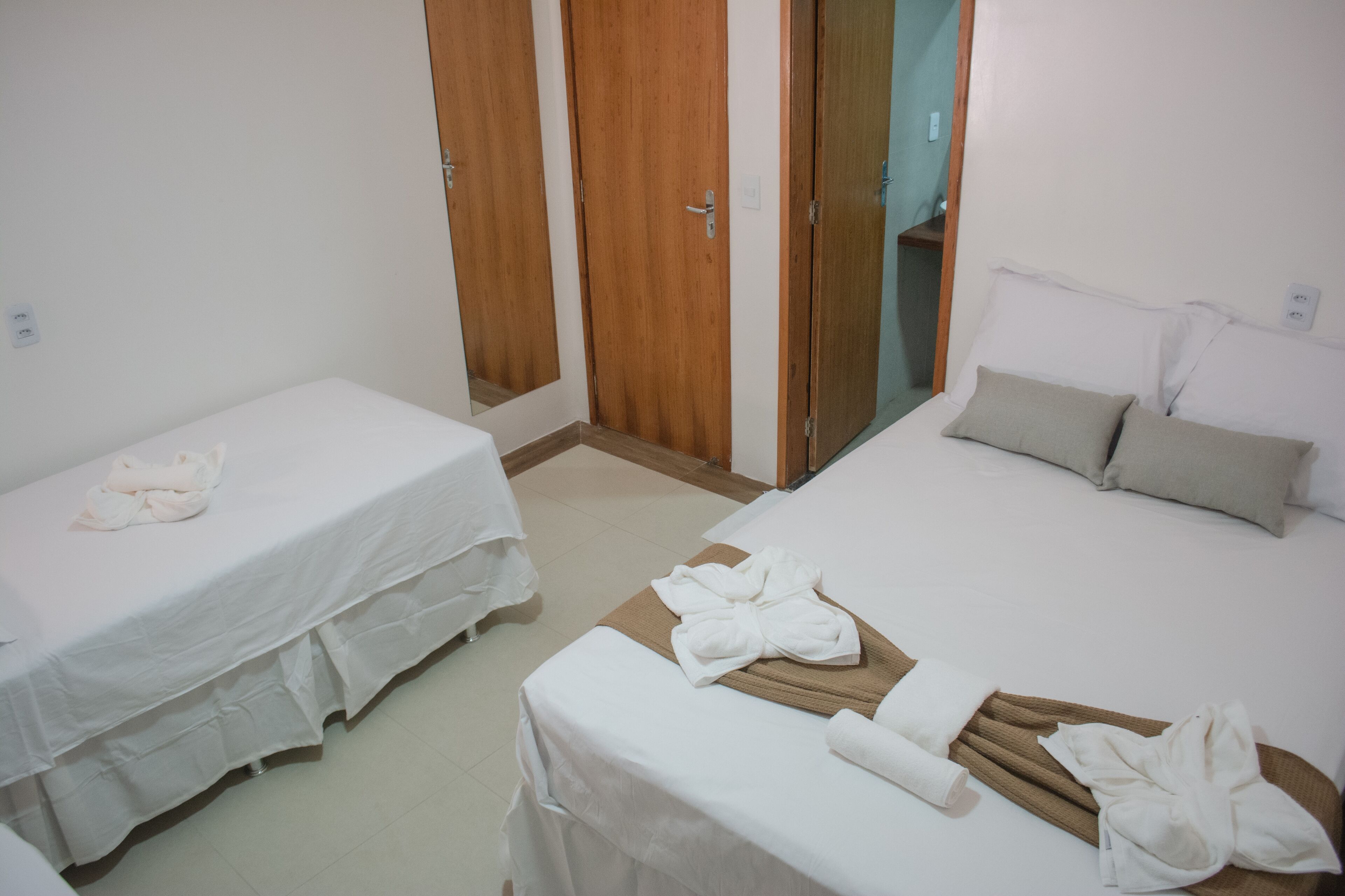 Une chambre d’hôtel avec deux lits, une armoire en bois et une salle de bain visible à travers une porte ouverte.