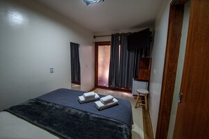 Habitación de hotel con cama, un taburete pequeño, televisión y puerta que da a un balcón.