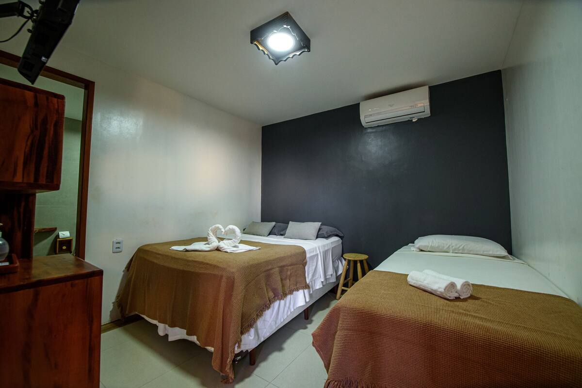 Ein Hotelzimmer mit zwei Betten, einem Holzschrank, einer Klimaanlage und einem kleinen Hocker.