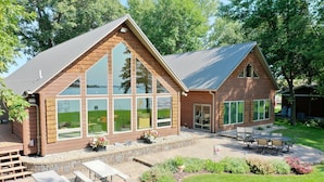 Une cabane en bois dotée de grandes fenêtres, une terrasse avec des tables et des chaises, et un jardin.