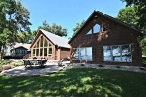 Une cabane en rondins dotée d’une grande fenêtre et d’un patio aménagé avec du mobilier d’extérieur.