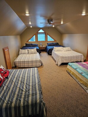 Une chambre avec trois lits, un ventilateur de plafond et des fenêtres de toit.