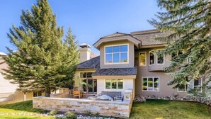 A two-story house with a stone patio, a covered outdoor seating area, and a large evergreen tree. - 1-10 N. Fairway Drive (Avon)