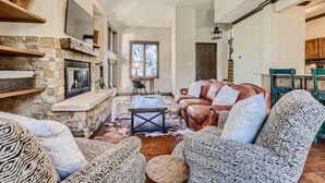 A cozy living room with a stone fireplace, leather sofa, patterned armchairs, and a rustic dining area. - 1-10 N. Fairway Drive (Avon)