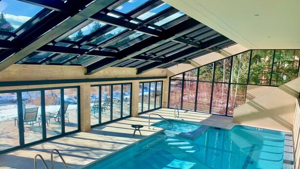 Una piscina interior con techo de cristal, vistas despejadas del paisaje circundante y un área de descanso con sillas.