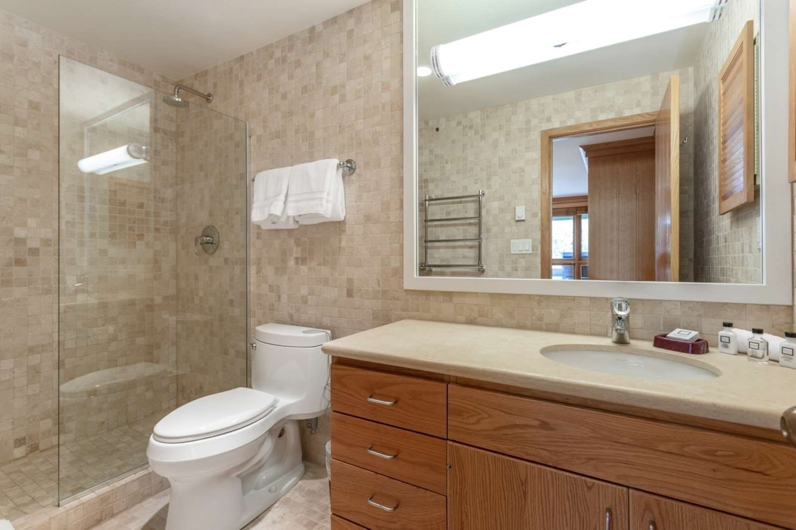 A bathroom with a glass shower enclosure, a toilet, a vanity with a sink, and a large mirror.