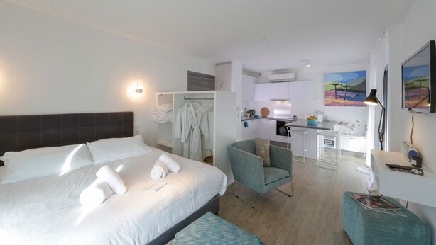 Ein modernes Hotelzimmer mit einem großen Bett, einer Sitzecke mit einem Sessel, einer Küchenzeile und einem Gemälde an der Wand.