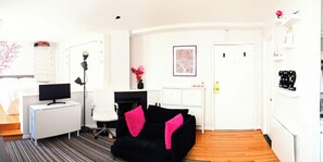 A modern living room with a black sofa, a white desk, and a computer monitor.