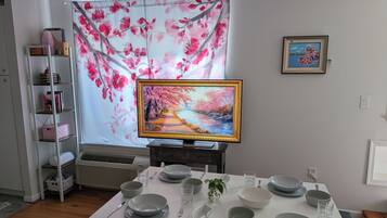 A dining area with a table set for four, a television displaying a landscape, and a bookshelf with various items.