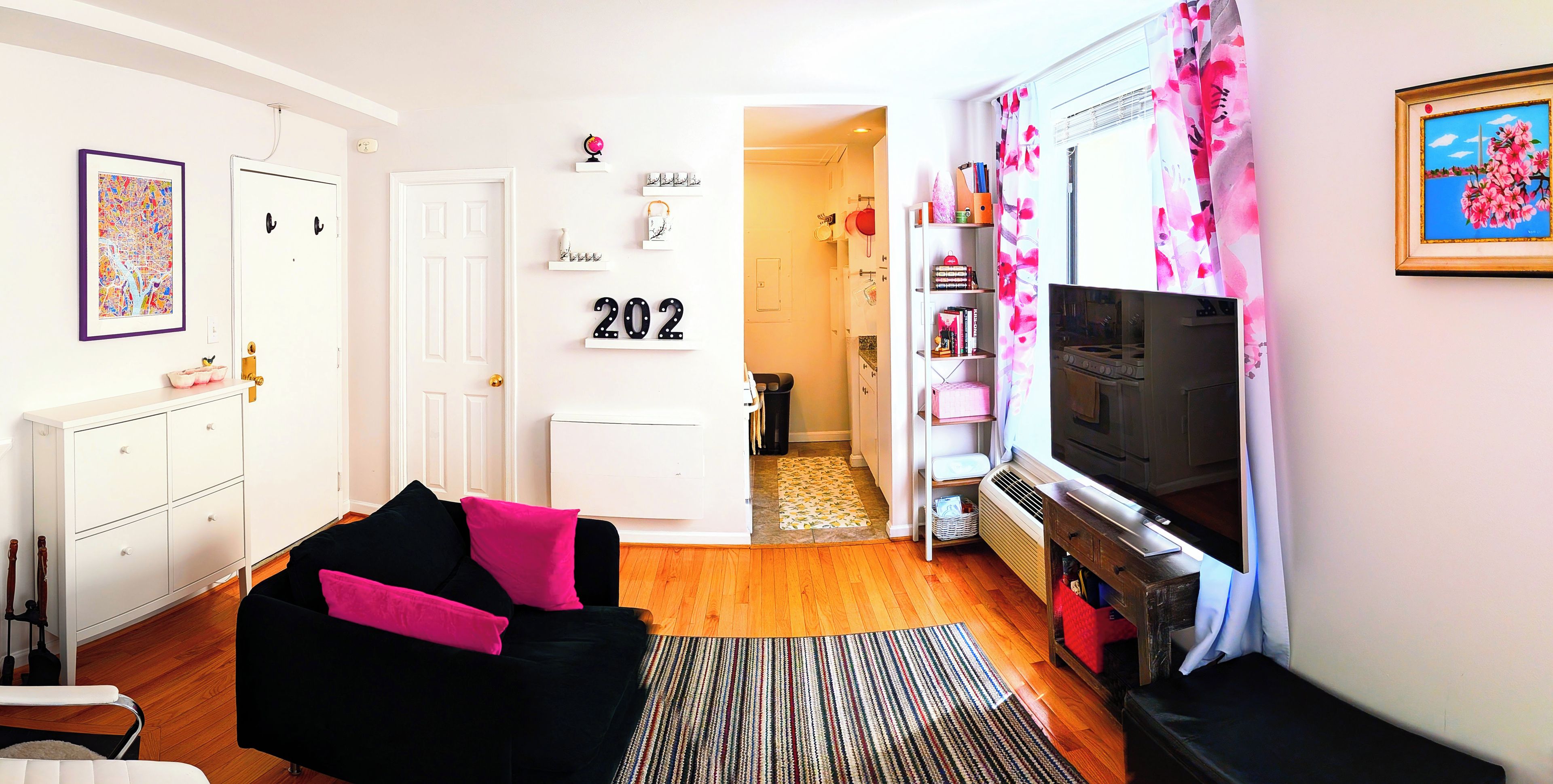 A living room with a black sofa, a television, and a kitchen area with a stove.