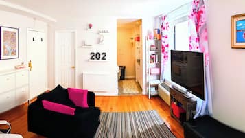 A living room with a black sofa, a television, and a kitchen area with a stove.