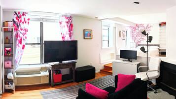 A modern living room with a flat-screen TV, a sofa, a chair, and a small table.