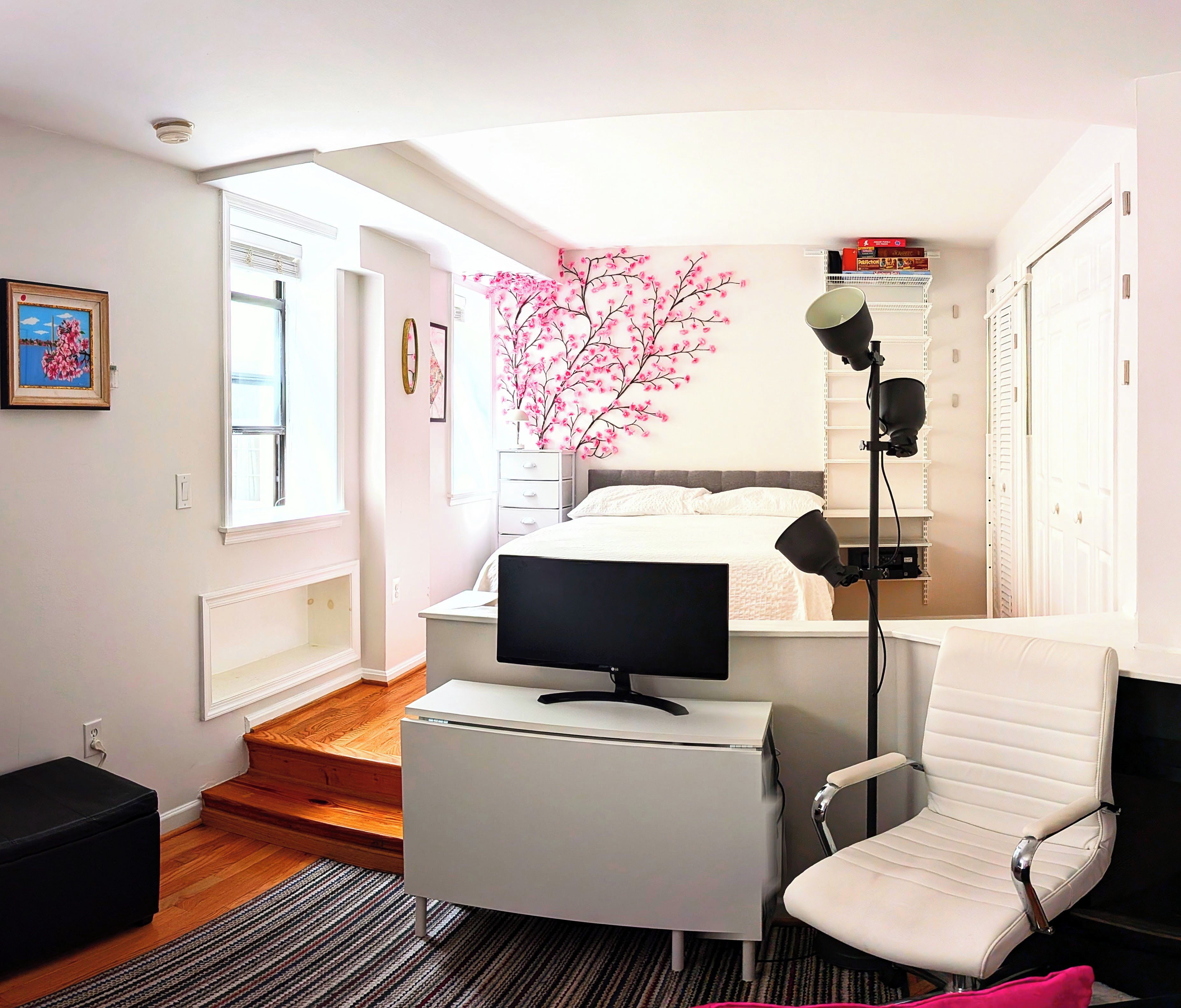 A modern bedroom with a bed, a TV, a desk, a chair, and a pink artificial tree.