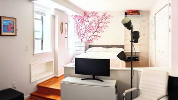A modern bedroom with a bed, a TV, a desk, a chair, and a pink artificial tree.