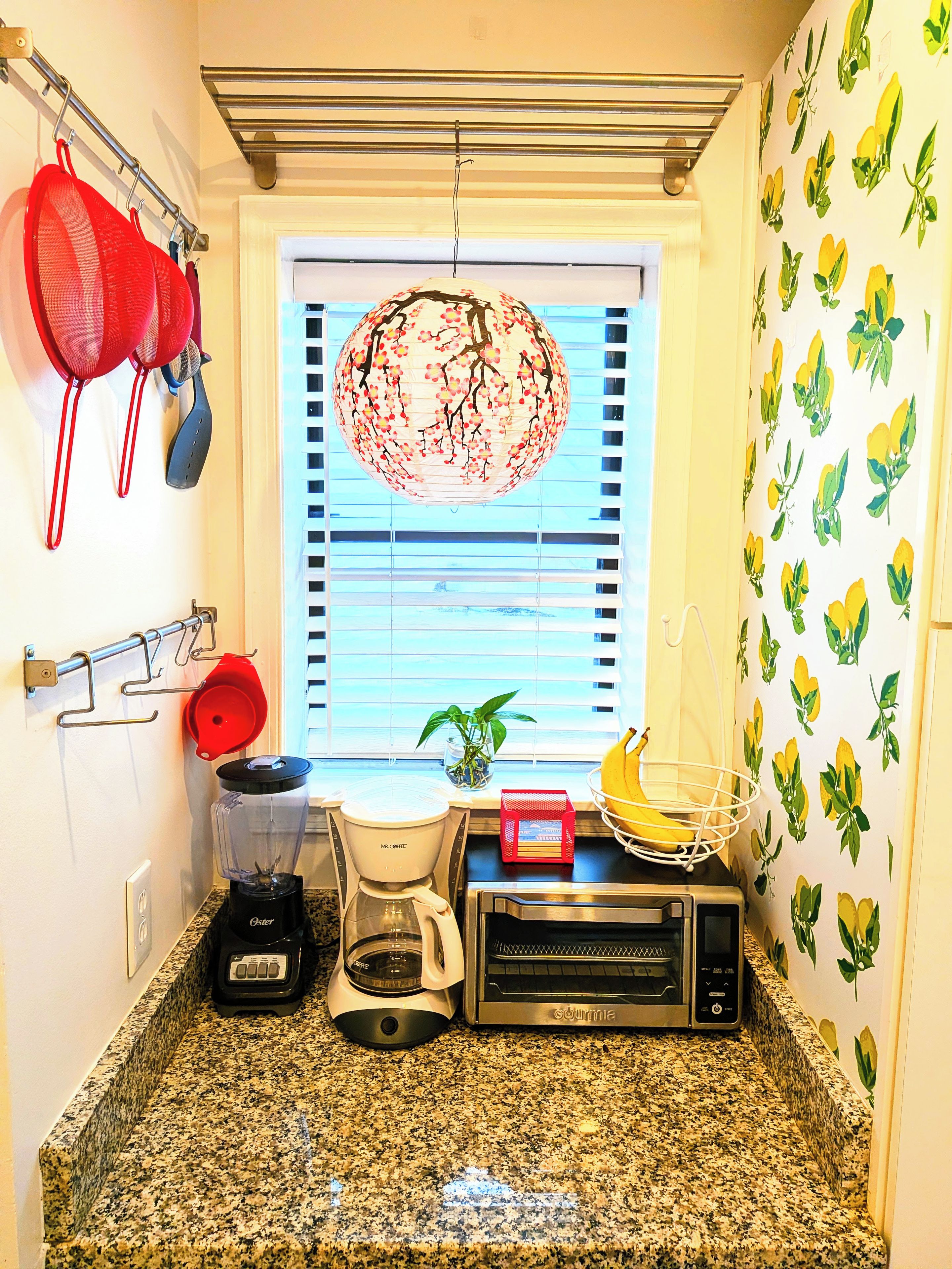 A kitchen with a window, a hanging light fixture, a coffee maker, a toaster, and a blender.
