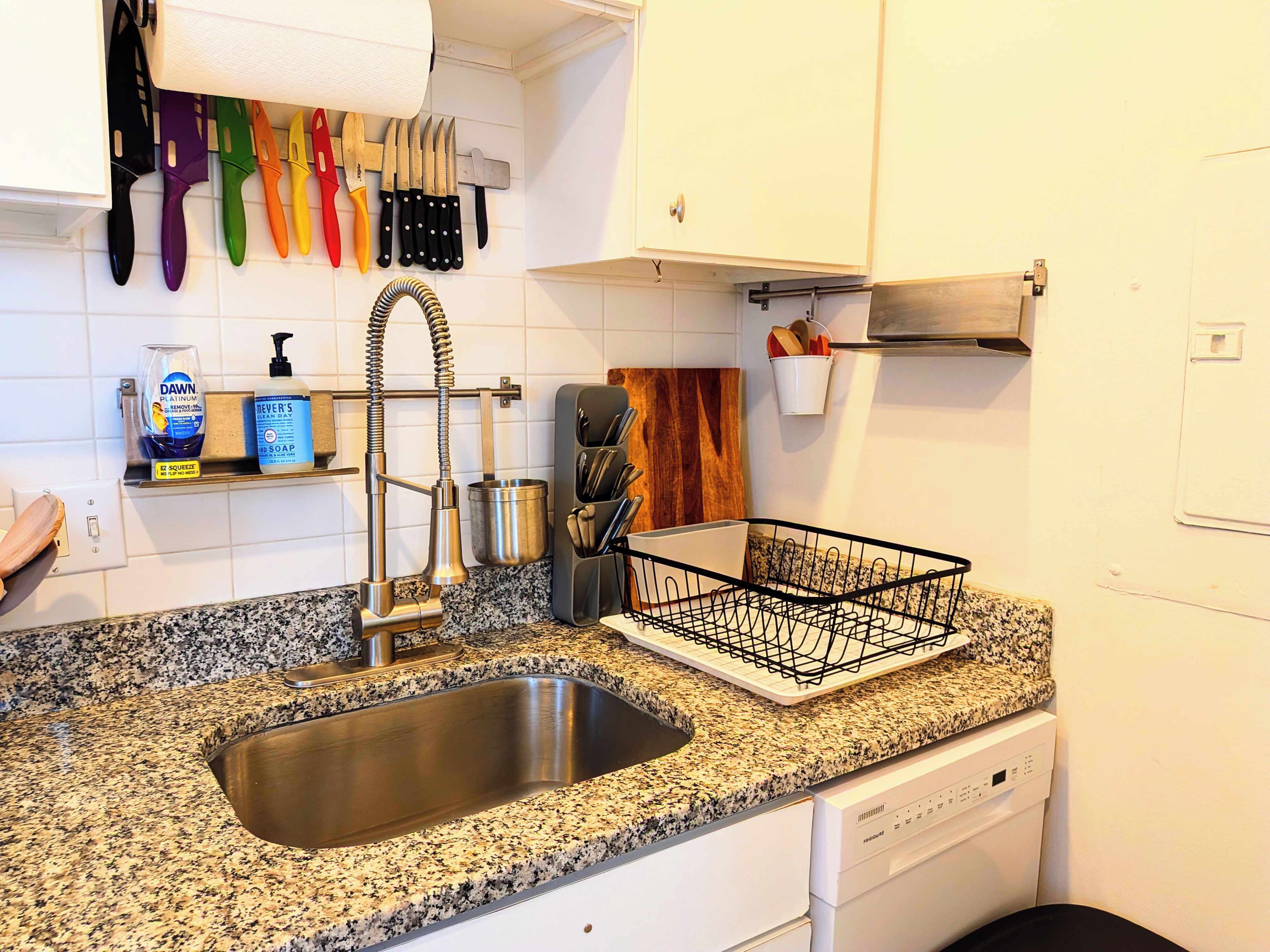 A kitchen with a stainless steel sink, a dish rack, and a variety of knives on the wall.