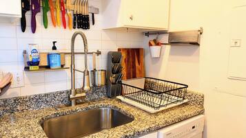 A kitchen with a stainless steel sink, a dish rack, and a variety of knives on the wall.