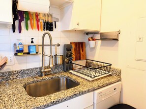A kitchen with a stainless steel sink, a dish rack, and a variety of knives on the wall.