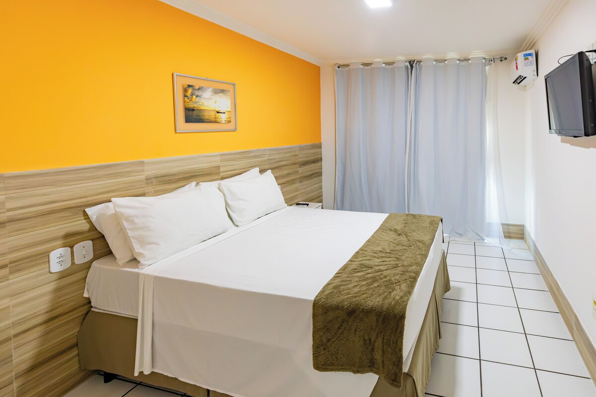 Quarto de hotel com uma cama, um quadro na parede, uma televisão e uma janela com cortinas.