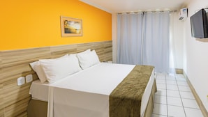 Ein Hotelzimmer mit Bett, einem Bild an der Wand, einem Fernseher und einem Fenster mit Vorhängen.
