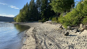 A sandy beach with footprints, a rocky shoreline, and dense green trees in the background.