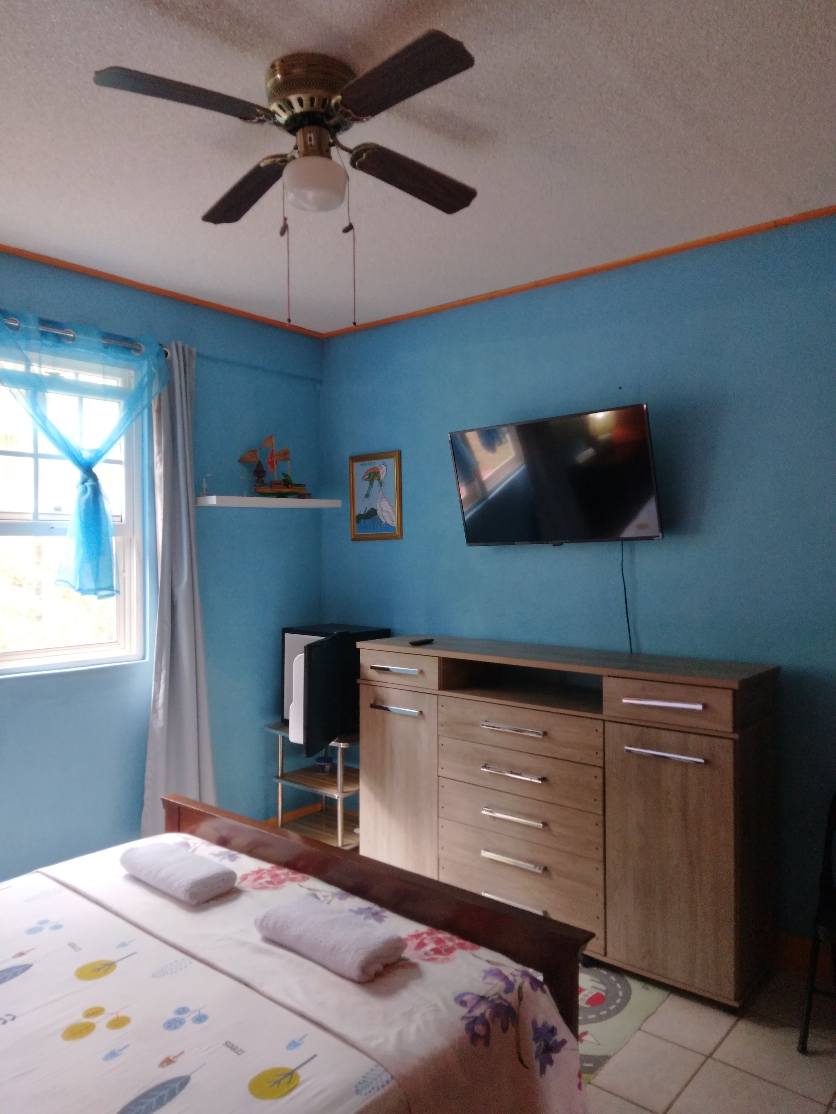 Un dormitorio con una cama, un escritorio, una silla, un televisor y un ventilador de techo.