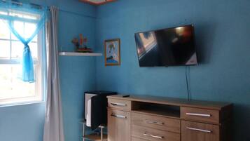 Un dormitorio con una cama, un escritorio, una silla, un televisor y un ventilador de techo.