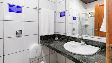 A bathroom with white tiled walls, a black marble countertop, a white sink, a hand dryer, and a wooden door.