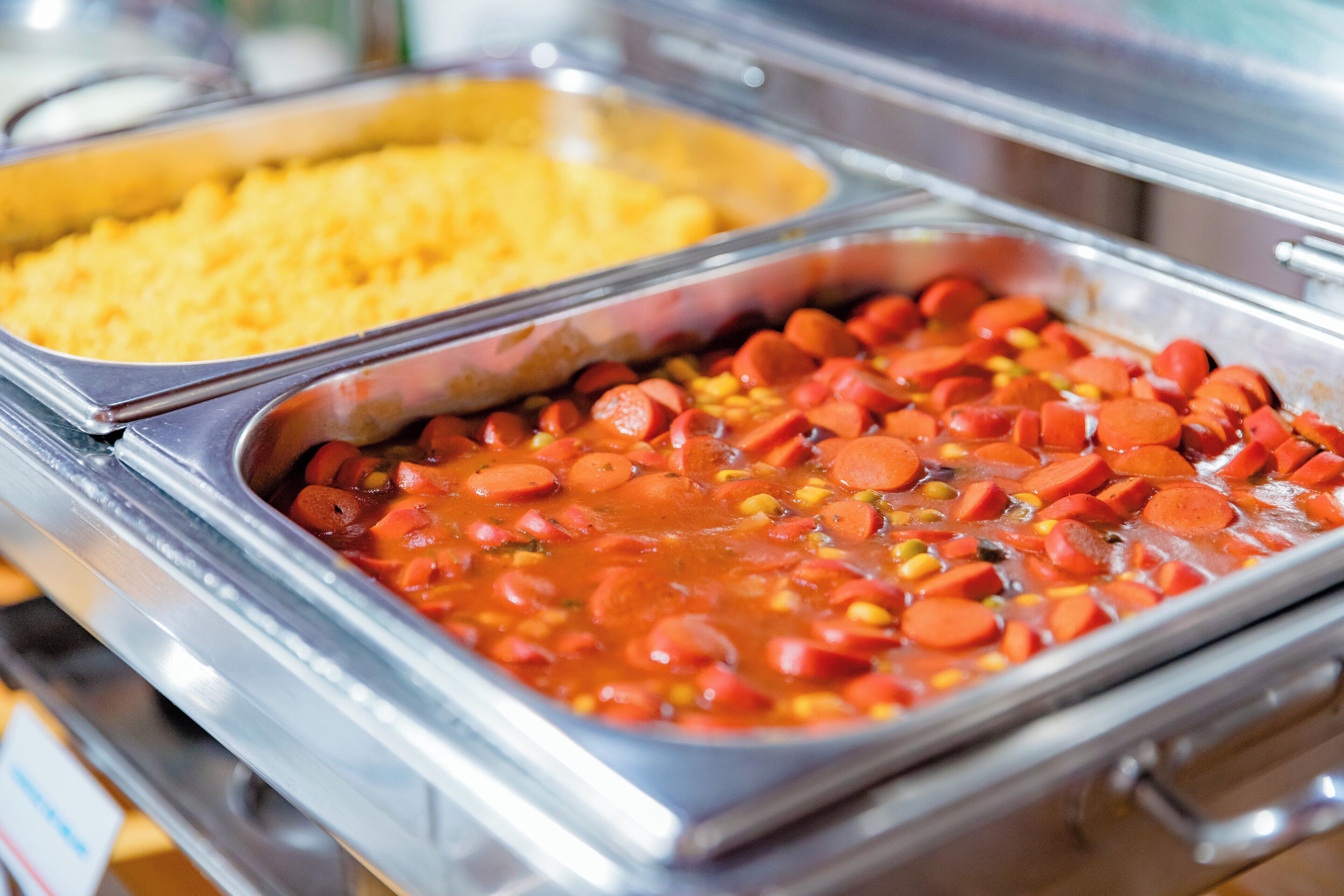 Un bufé con una variedad de platos, incluyendo un recipiente grande de salchichas en rodajas y un bol de arroz amarillo.