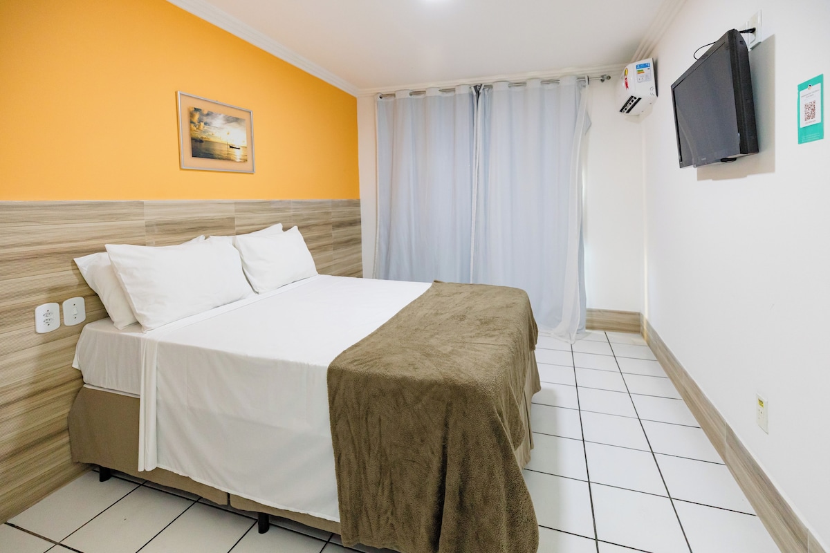 Une chambre d’hôtel équipée d’un lit, d’une télévision, d’une fenêtre avec des rideaux et d’un climatiseur fixé au mur.