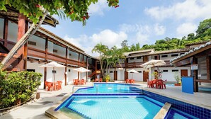 A swimming pool with blue tiles, surrounded by outdoor seating and a building with wooden balconies. - Hotel Casa Blanca Porto Seguro (Porto Seguro)