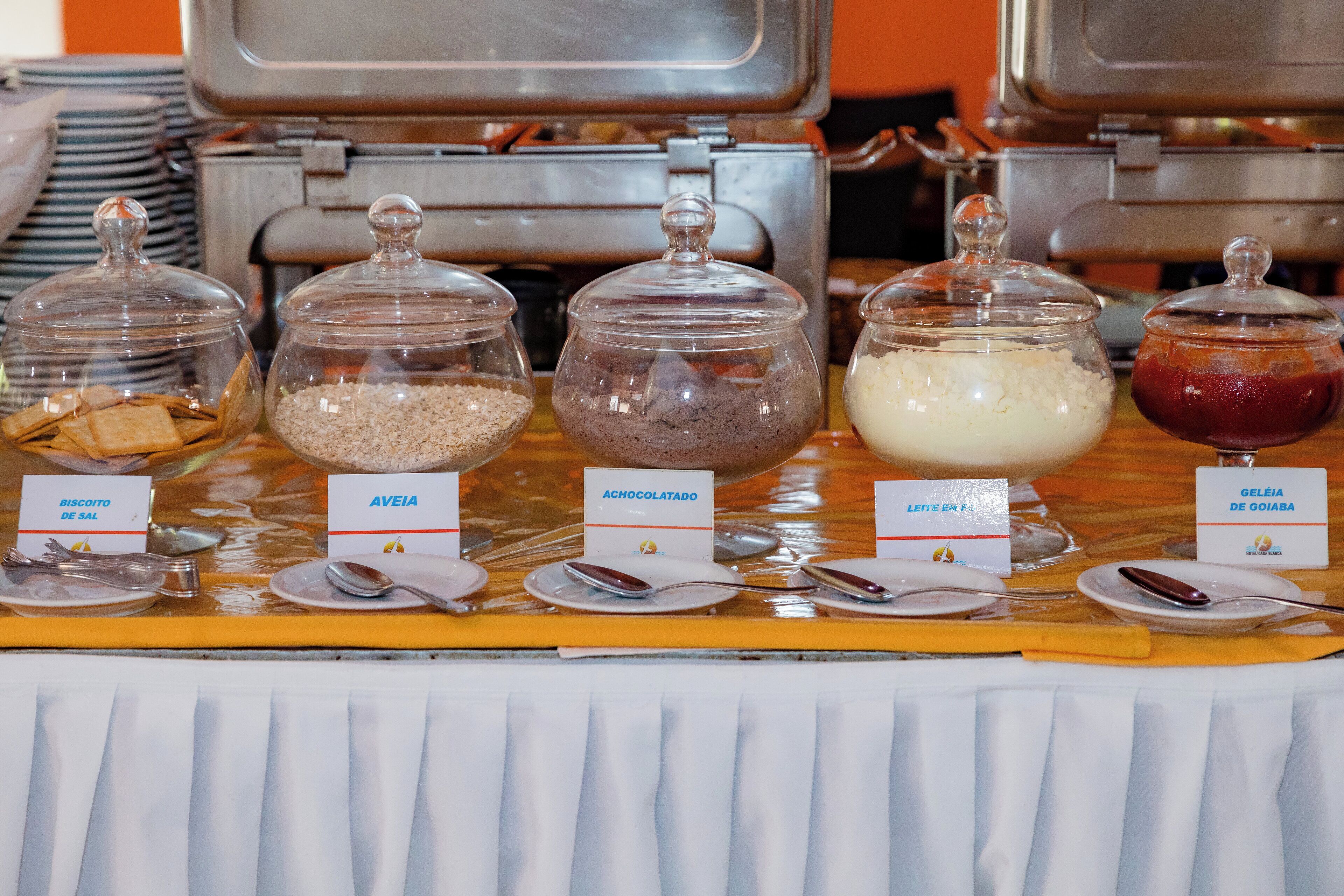 Una mesa de buffet con alimentos etiquetados, entre ellos, galletas, queso, chocolate, leche y mermelada.