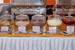Una mesa de buffet con alimentos etiquetados, entre ellos, galletas, queso, chocolate, leche y mermelada.
