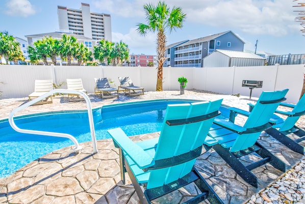 A swimming pool with lounge chairs, a palm tree, and buildings in the background.