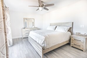 A bedroom with a bed, nightstands, a mirror, and a ceiling fan.