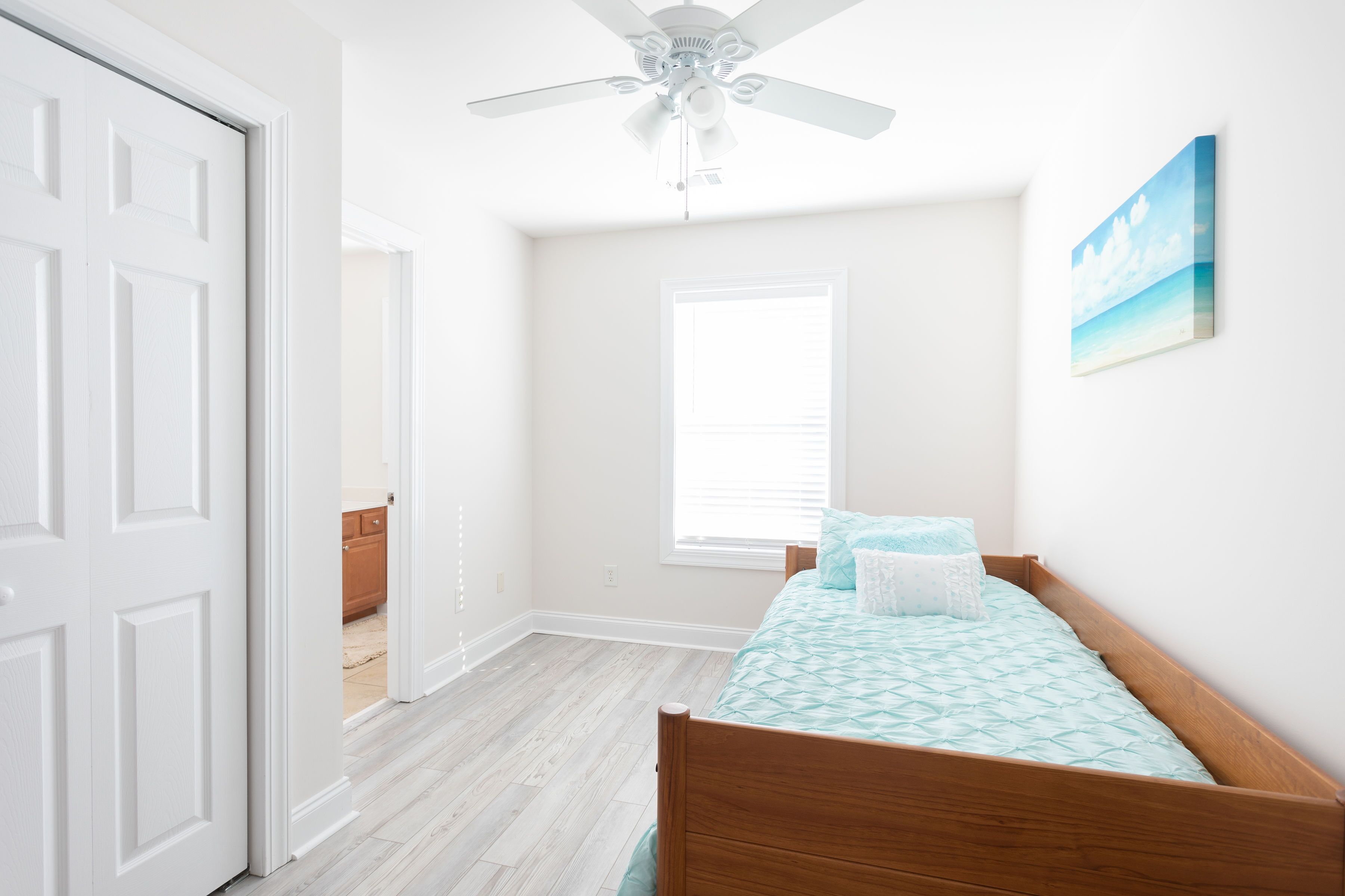 A bedroom with a wooden bed, a ceiling fan, a window, and a painting on the wall.