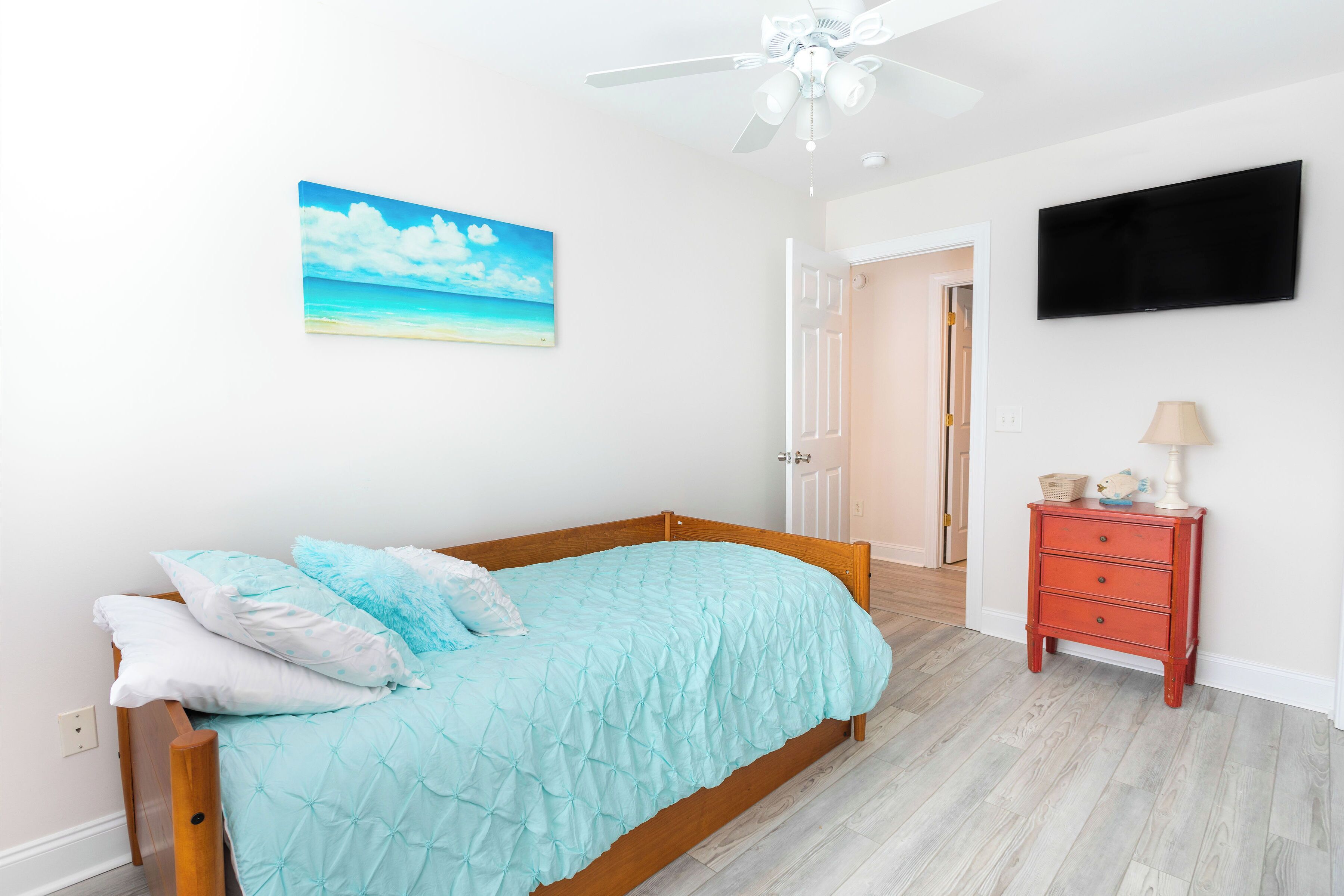 A bedroom with a bed, a ceiling fan, a painting, a TV, and a nightstand.