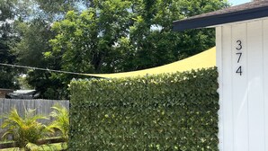 A white building with the number 374 on its side, surrounded by a lush green hedge and a yellow tarp.