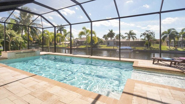 Una piscina interior con agua cristalina, rodeada por un recinto de vidrio, y vistas a una zona residencial con palmeras y casas.