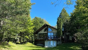 A two-story house with a large balcony, surrounded by lush greenery and a clear blue sky.