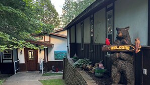 A building with a stone wall and a welcome sign featuring a bear statue.