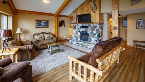 A rustic living room with a stone fireplace, wooden furniture, and a mounted deer head.