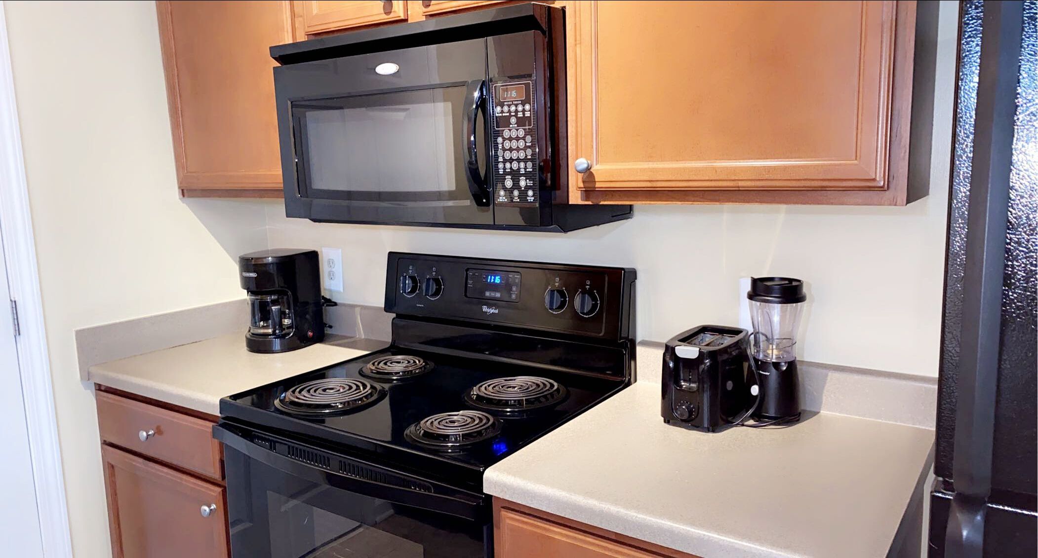 A kitchen with a black stove, a microwave, a coffee maker, and a blender.