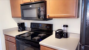 Une cuisine équipée d’une cuisinière noire, d’un four à micro-ondes, d’une machine à café et d’un mixeur.