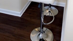 Deux tabourets de bar blancs, avec des pieds en chrome, sont placés dans un coin d’une pièce dont le sol est en bois et les murs sont blancs.