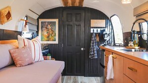 Un interior acogedor con una cama, un cuadro, una zona de cocina y una puerta con un cartel de bienvenida.
