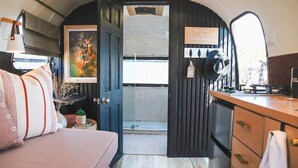 Un interior acogedor de autocaravana con cama, kitchenette y una puerta que da a un espacio exterior.