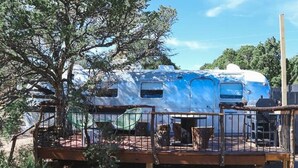 Una casa rodante con terraza, rodeada de árboles y un cielo despejado.