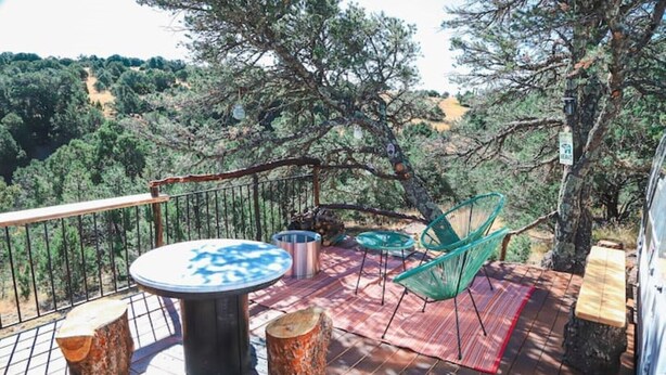 Una terraza de madera con una mesa y sillas, rodeada de árboles y vistas al campo.