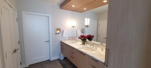 A modern bathroom with a large mirror, a marble countertop, and a vase of red flowers. - Full Beach View 2 Bedroom Penthouse (Longboat Key)